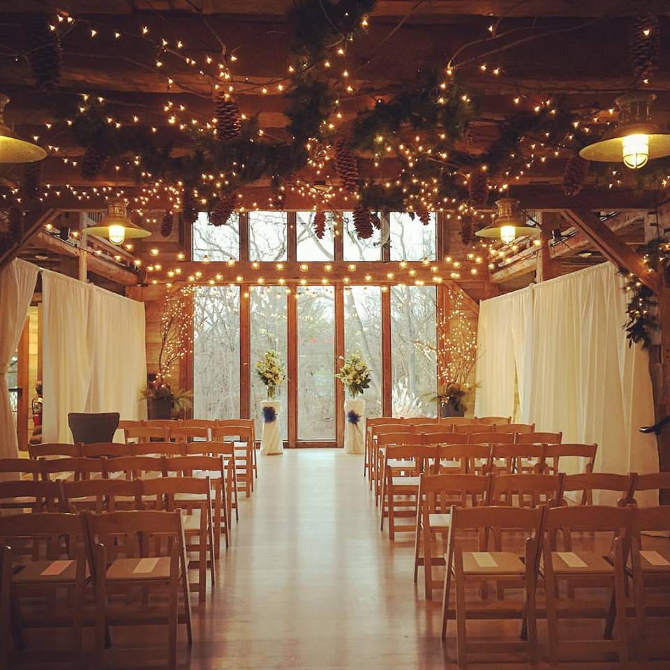 Indoor ceremony setup at Pat's Barn with chairs, aisle, lights, pinecones and other greenery. 
