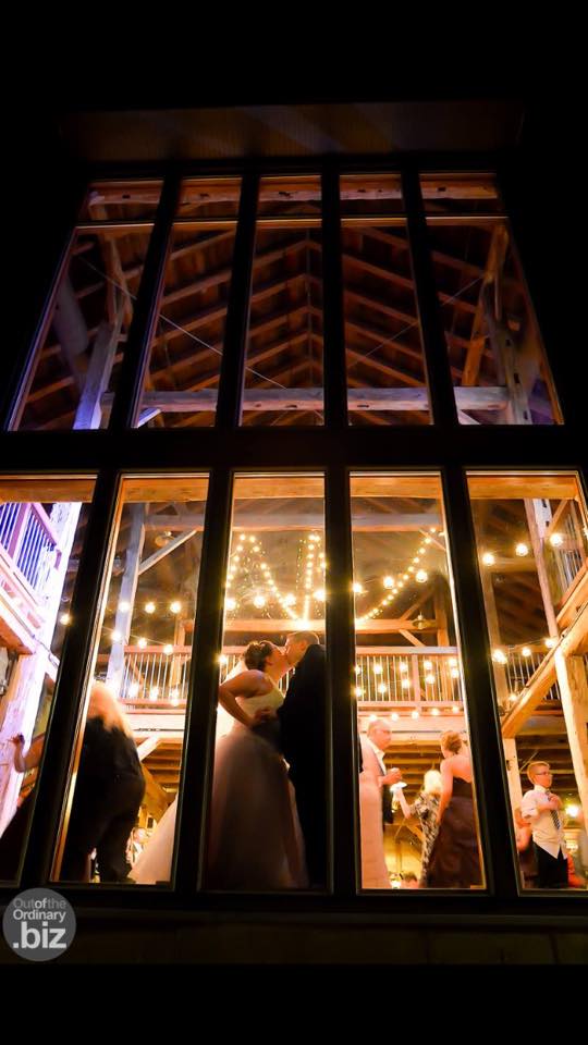 Bride and groom sharing a kiss in front of a big window at night inside Pat's Barn. 