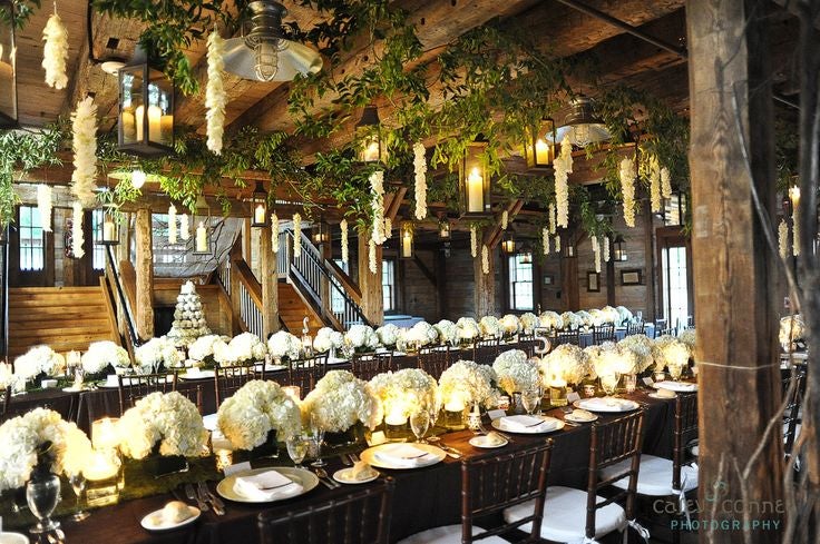 Inside of Pat's Barn showing greenery and lights decorating theceiling over decorated dining tables. 